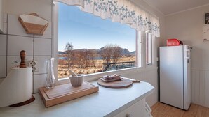 A kitchen with a large window, a wooden cutting board, a bowl, and a red appliance. - Holiday house with perfect location (Vestvågøy)