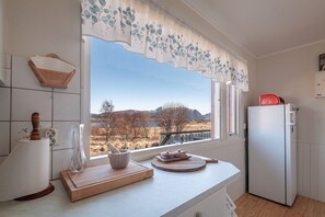 Et køkken med et stort vindue, en træ skærebræt, en skål og en rød apparat.