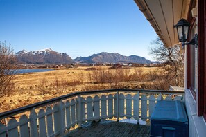 En træterrasse med hvid gelænder, en blå køleboks og udsigt til et bjerglandskab og et vandområde.