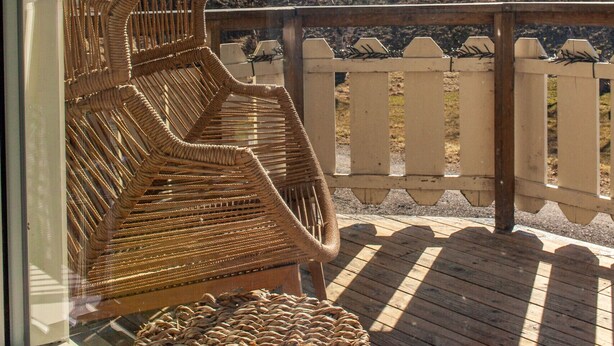 A wicker chair and a woven basket on a wooden deck with a view of mountains and a fence. - Holiday house with perfect location (Vestvågøy)