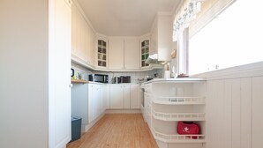 A kitchen with white cabinets, a microwave, a kettle, and a red first aid kit on a shelf. - Holiday house with perfect location (Vestvågøy)