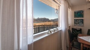 A room with a window overlooking a mountainous landscape, a dining area with a table and chairs, and a wall-mounted lamp. - Holiday house with perfect location (Vestvågøy)