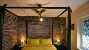 A room with a brick wall, a canopy bed, two bedside tables with lamps, and a decorative ceiling light.