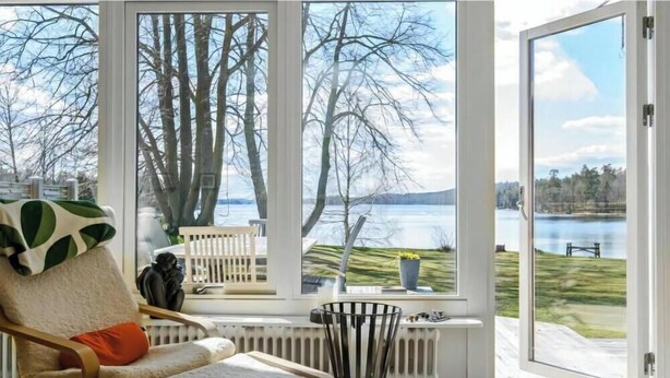 Huoneessa on suuri ikkuna, josta avautuu näkymä järvelle, sekä tuoli, patteri ja pieni pöytä, jonka päällä on kasvi.