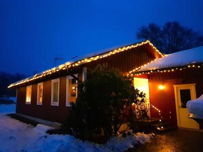 A house with a snow-covered roof and a porch, illuminated by string lights.