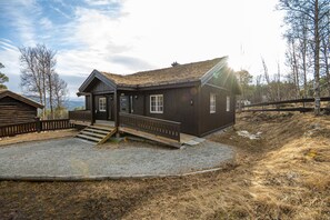 A wooden cabin with a gravel driveway and a wooden deck.