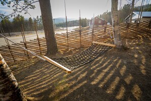 A hammock between trees, a wooden fence, and a red building in the background.