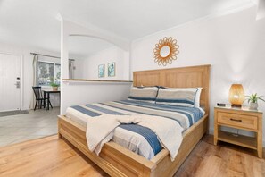 A bedroom with a wooden bed, a bedside table with a lamp, and a window with blinds. - Updated, Excellant Location Walk to Beach~Pool~Free Parking - Pelican Pointe 113 (Clearwater)