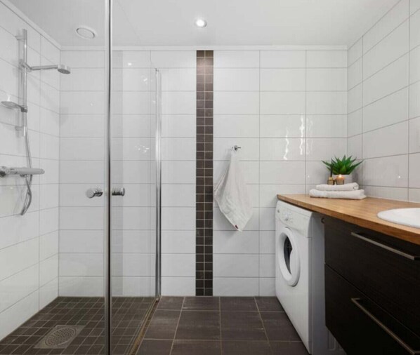 Un baño moderno con cabina de ducha de vidrio, lavadora y encimera de madera.