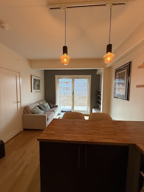 Una cocina moderna con una isla de madera, luces colgantes, un sofá y un ventanal grande.