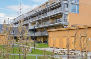 Un edificio residencial de varios pisos con balcones, un espacio exterior cubierto y una zona de estacionamiento para bicicletas.