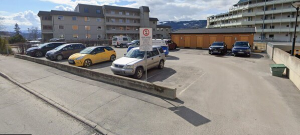 Ein Parkbereich mit mehreren Autos, einem Schild für privaten Stellplatz und Gebäuden im Hintergrund.