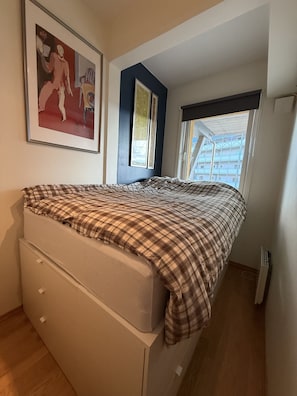 Un dormitori amb un llit, una petita taula de nit, una finestra i un quadre a la paret.