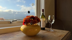 Eine gelbe Vase mit Blumen auf einem Holztisch neben einem Fenster.
