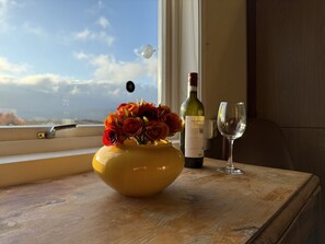 Un jarrón amarillo con flores sobre una mesa de madera junto a una ventana.