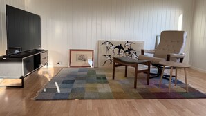 Ein Wohnzimmer mit einem Flachbildfernseher, einem gerahmten Bild, einem Sessel und einem farbenfrohen Teppich.