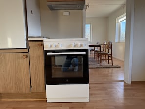 Keittiössä on valkoinen ja musta Electrolux-uuni, puukehikoiset kaapit sekä ruokailutila, jossa on tuoleja ja pöytä.