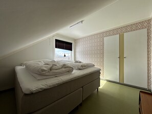 A bedroom with a bed, a window with blinds, a wardrobe, and patterned wallpaper. - Charming house close to Leknes (Vestvågøy)