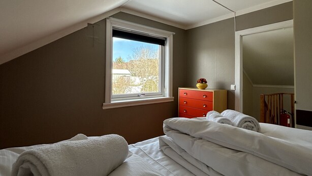 Ein Schlafzimmer mit Bett, Fenster, Kommode und Spiegel.