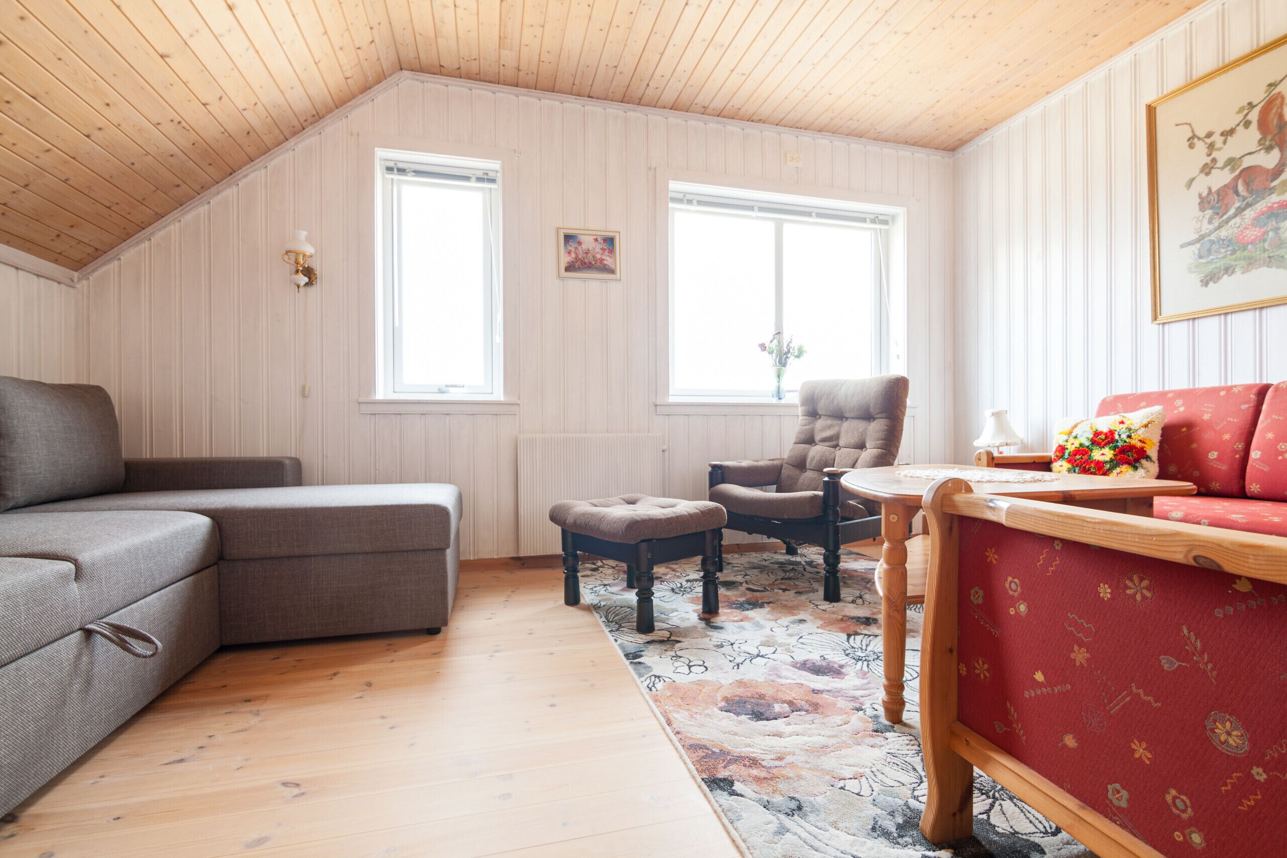 A cozy room with a sloped ceiling, wooden walls, a sofa, a chair, a small table, and a rug.