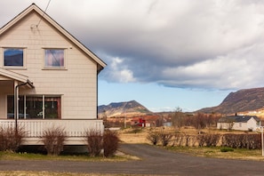 Une maison à deux étages avec un porche, une allée et un paysage montagneux en arrière-plan.