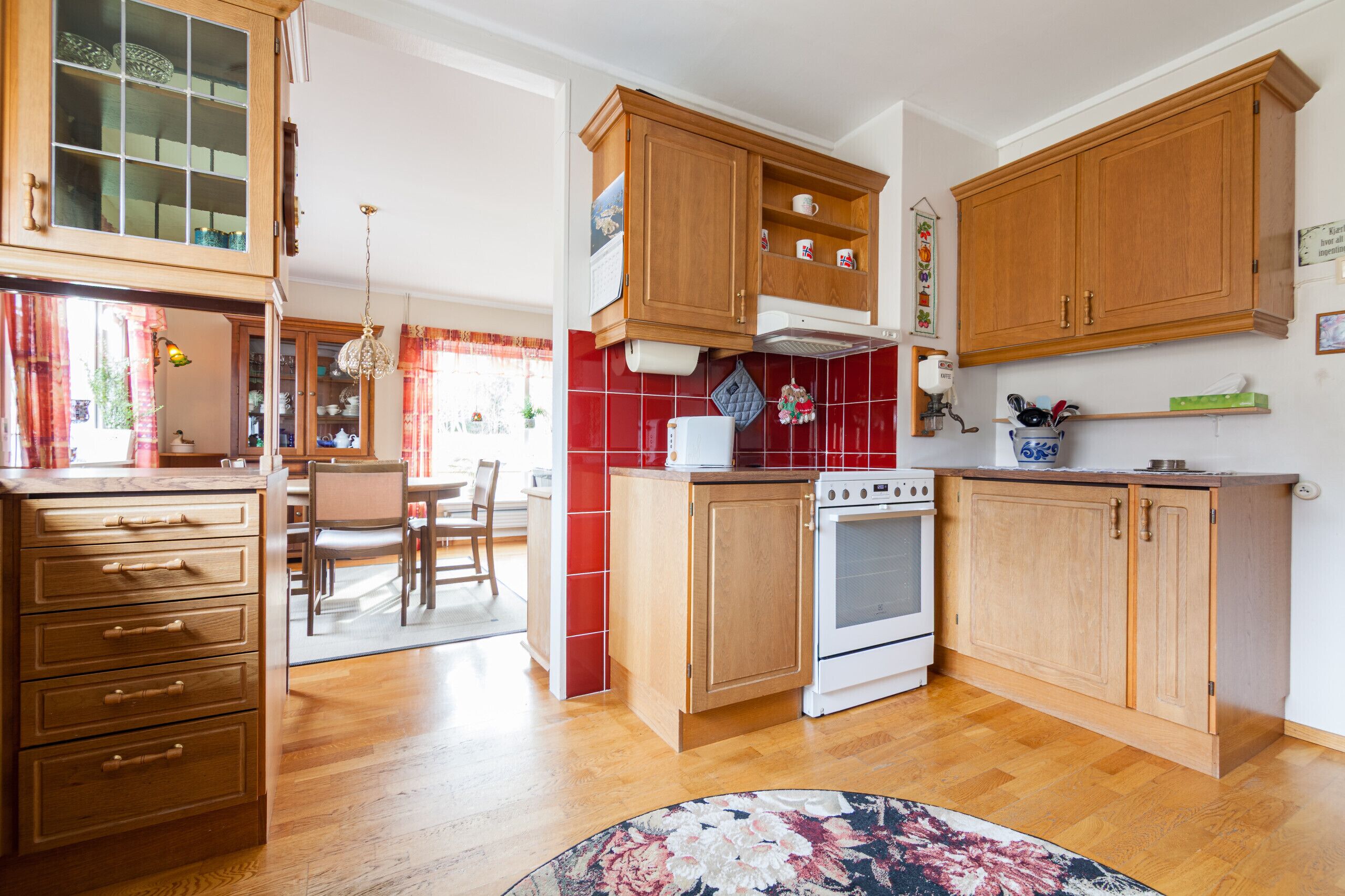 Een keuken met houten kastjes, een fornuis en een eethoek met stoelen.
