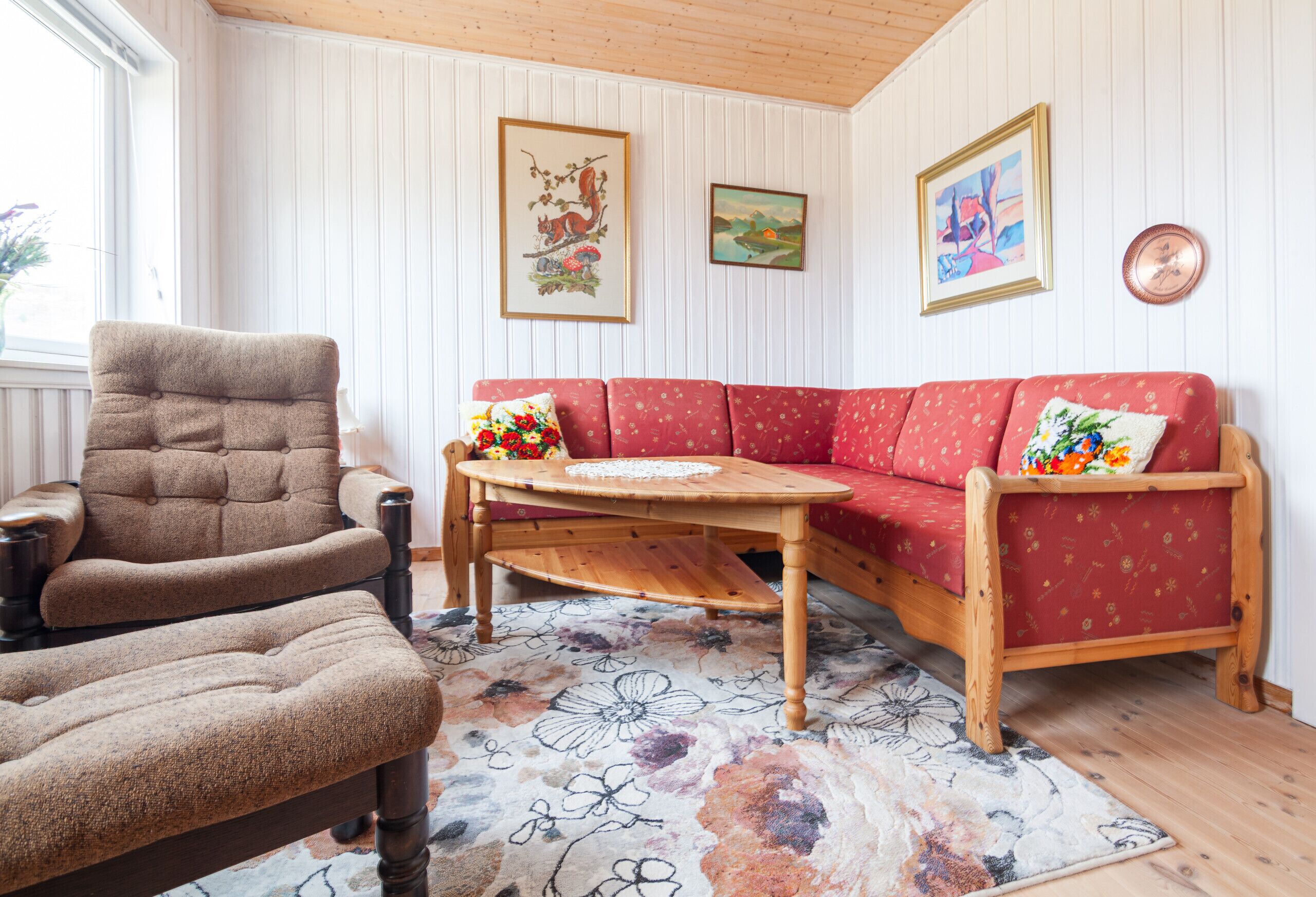 A room with a red sofa, a wooden armchair, a wooden coffee table, and a floral rug.