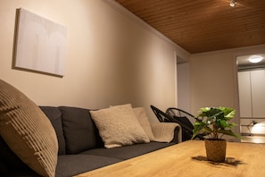 Un salon moderne avec un plafond en bois, un canapé foncé agrémenté de coussins beige, une petite table en bois et une plante en pot.