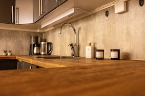 Una cocina con un lavamanos de acero inoxidable, una cafetera y dos velas sobre la encimera.