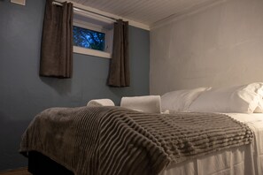 Une chambre à coucher avec un lit, des oreillers blancs, une fenêtre avec des rideaux et une vue sur les arbres à l’extérieur.