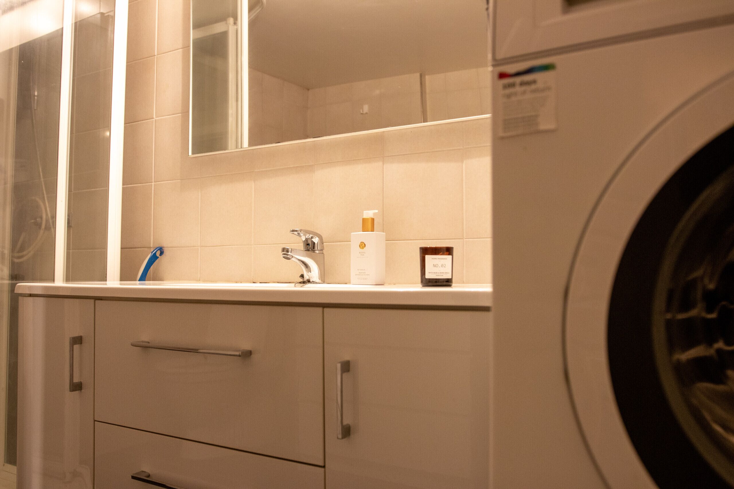 A bathroom with a washing machine, a mirror, and a sink with a faucet.