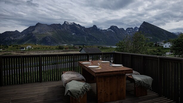 A wooden deck with a table set for dining, overlooking a mountainous landscape.
