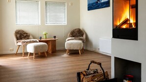 A living room with two armchairs, a small round table, a fireplace, and a painting of a boat on the wall.