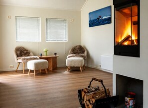 A living room with two armchairs, a small round table, a fireplace, and a painting of a boat on the wall. - Fredly, beautiful home in Fredvang (Flakstad)