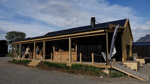 A wooden building with a covered porch, a chimney, and a flag.