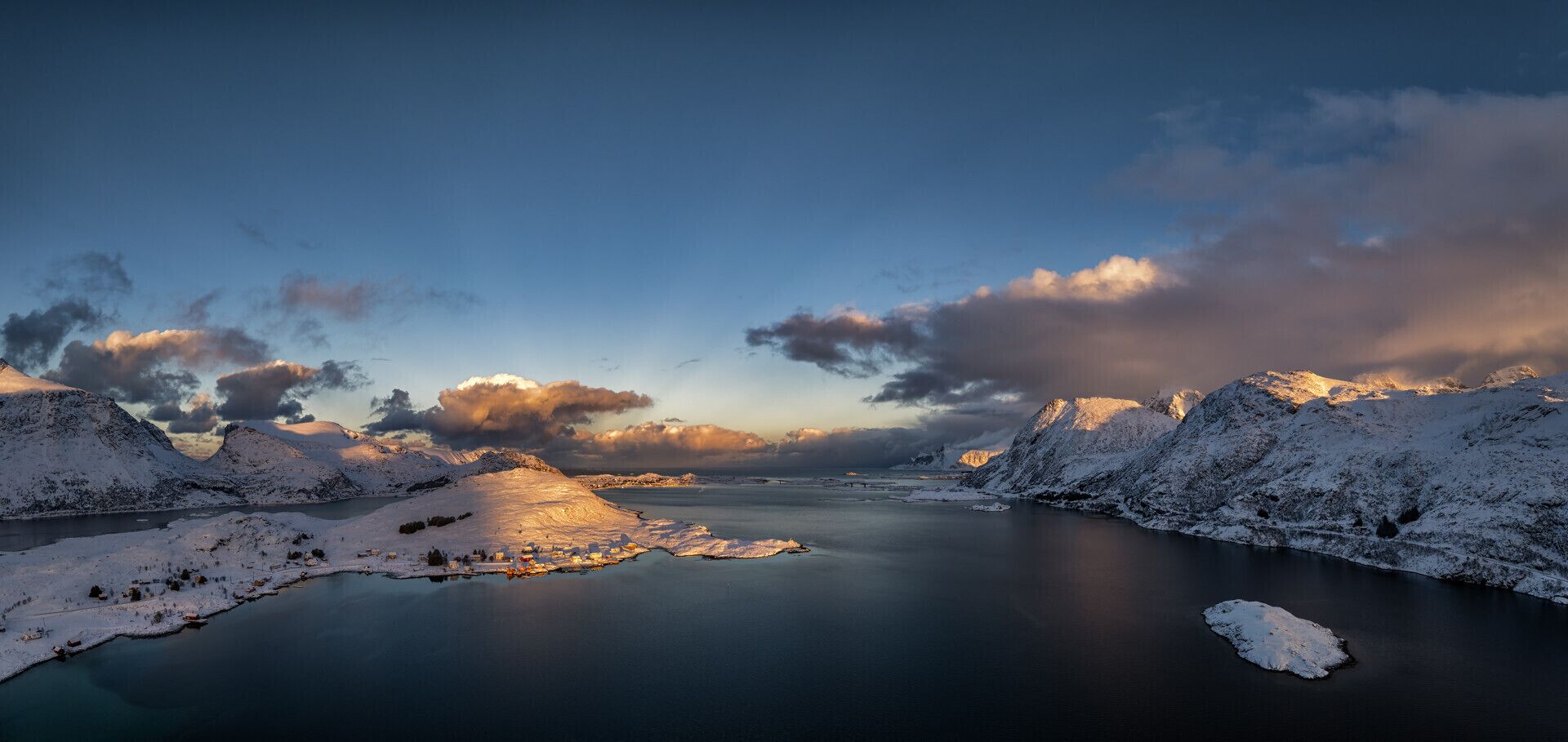 Ein weitreichender Blick auf eine verschneite Landschaft mit einem stillen See, Bergen und einem klaren Himmel.