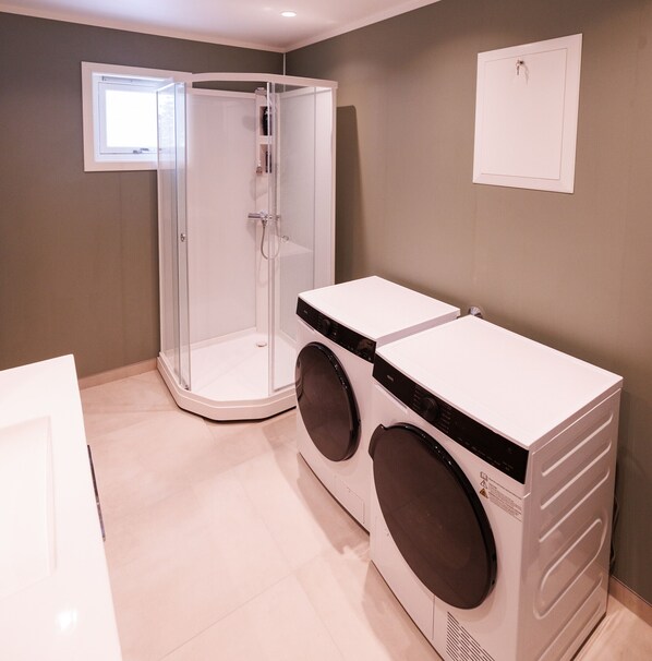 Un área de lavandería con lavadora y secadora, cabina de ducha con mampara de vidrio y un ventanal.