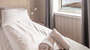 Una cama con cabecera, una ventana con cortinas y vista al mar.