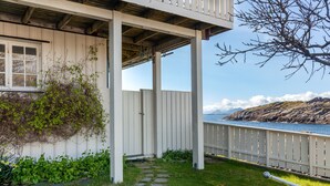 Una casa costera con balcón, un sendero de piedra y vista al mar.