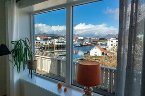 A room with a large window overlooking a harbor, a potted plant, and a lamp on the windowsill. - House in Henningsvær with amazing views (Vågan)
