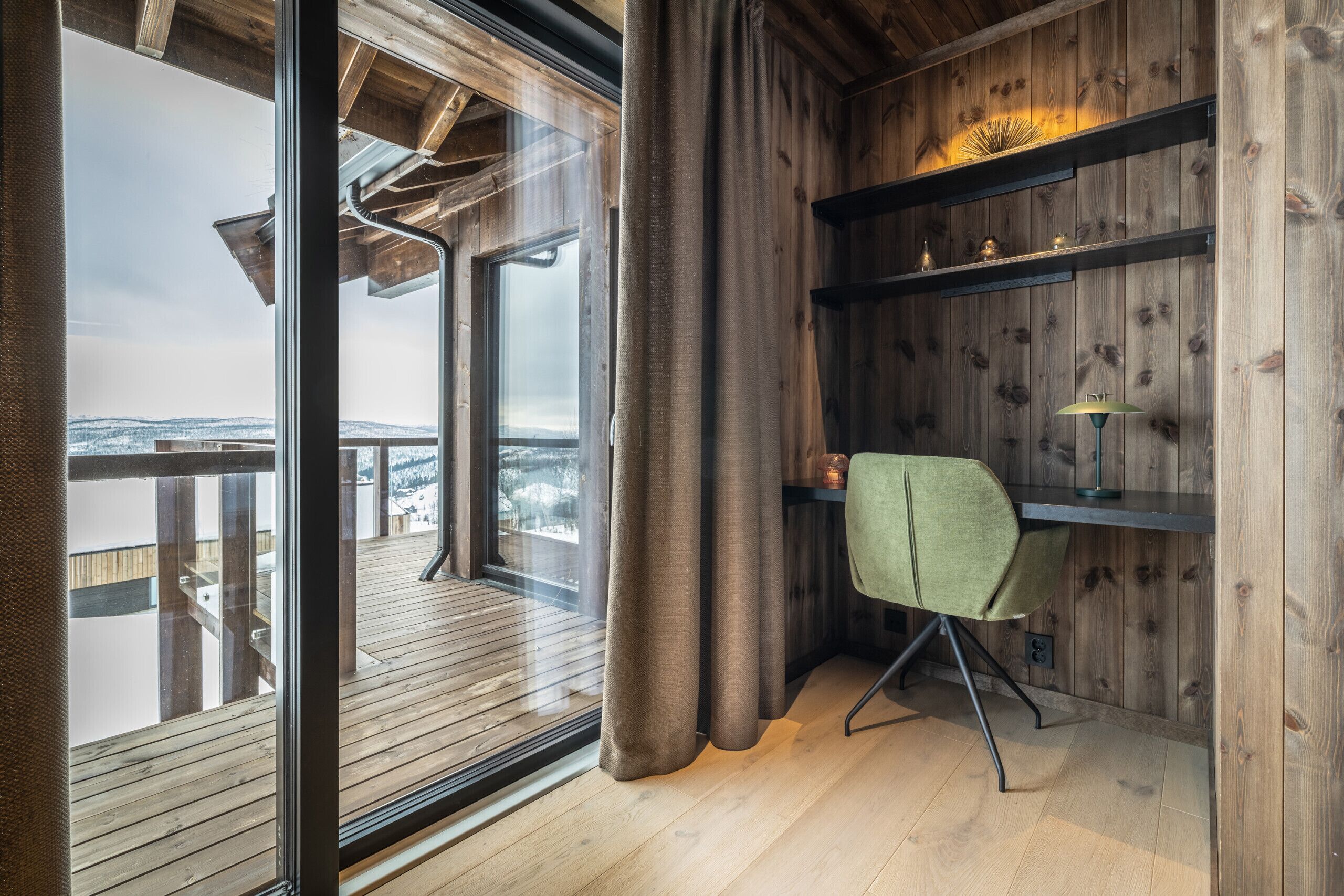 Ein Zimmer mit großem Fenster, Holzwänden, einem Schreibtisch mit Stuhl und einem Regal mit Dekorationen.