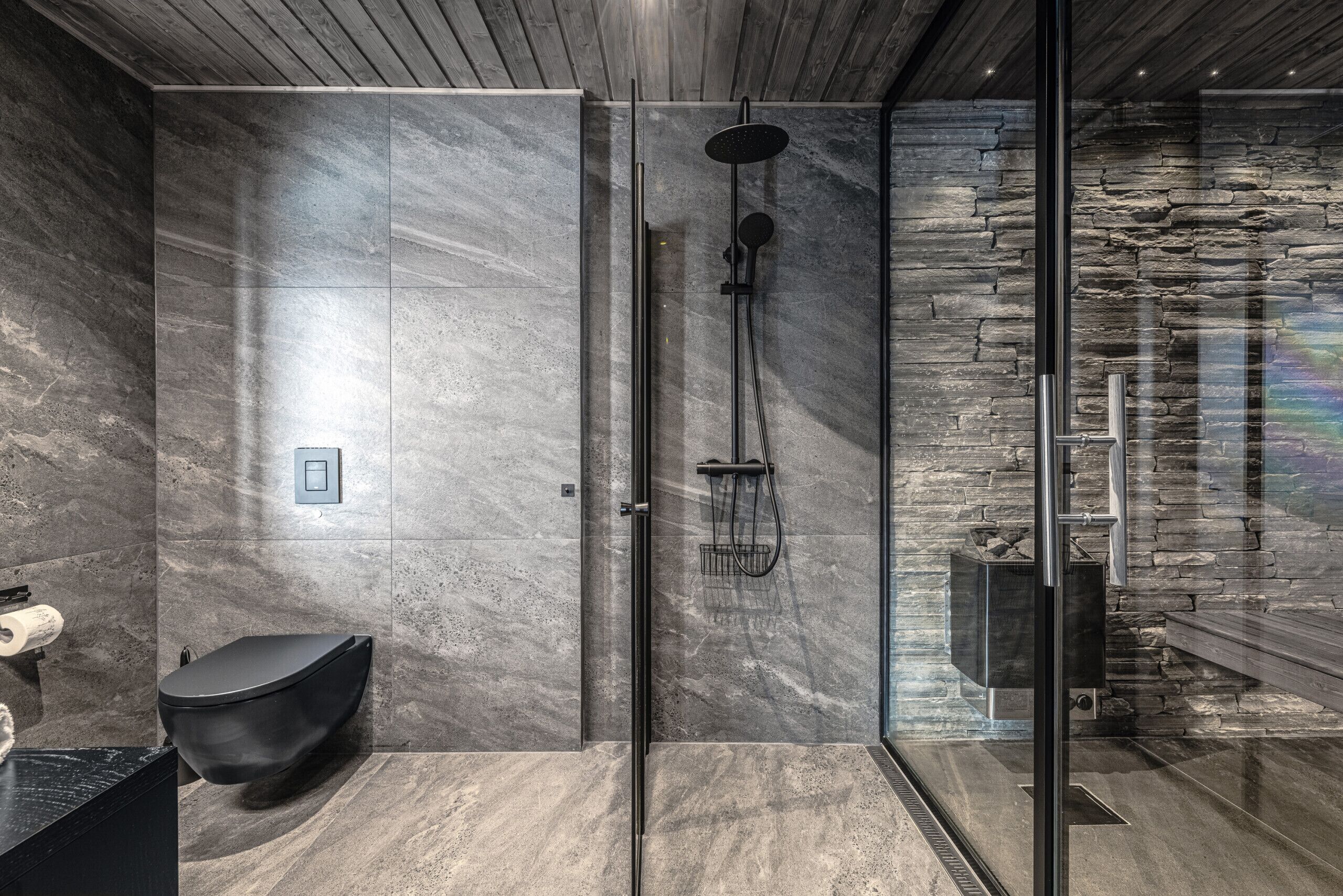 Ein modernes Badezimmer mit Duschkabine aus Glas, einer schwarzen Toilette und einer Steinwand.