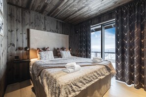 A wooden-paneled room with a large bed, a nightstand, and a window with curtains.