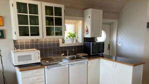 Una cocina compacta con muebles blancos, un microondas, un tostador y un lavamanos.
