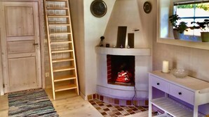Una habitación con puerta y escalera de madera, chimenea, una consola blanca y una ventana con plantas.