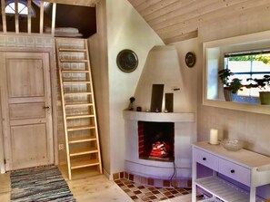 Ein Zimmer mit Holztür, einer Holzleiter, einem Kamin, einem weißen Konsolentisch und einem Fenster mit Pflanzen.