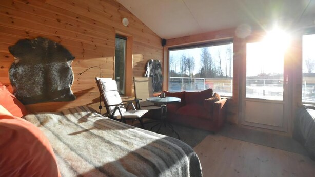 A cabin with a bed, a chair, a table, and a large window.