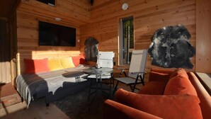A wooden cabin interior with a bed, sofa, table, and a painting on the wall.