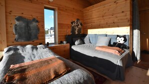 A wooden cabin room with two beds, a window, and a bear hide on the wall.