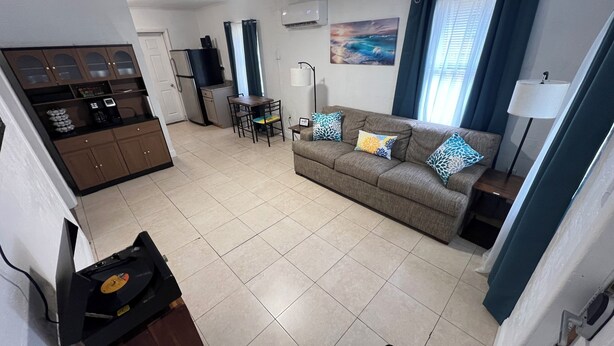A living room with a sofa, a coffee table, a dining table, and a kitchen area with cabinets and appliances. - Space Coast getaway! The Yellow Sunrise! 2 bed 1 bath Oasis (Merritt Island)